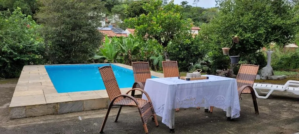Piscina do Pendotiba Hostel com mesa e vegetação ao fundo